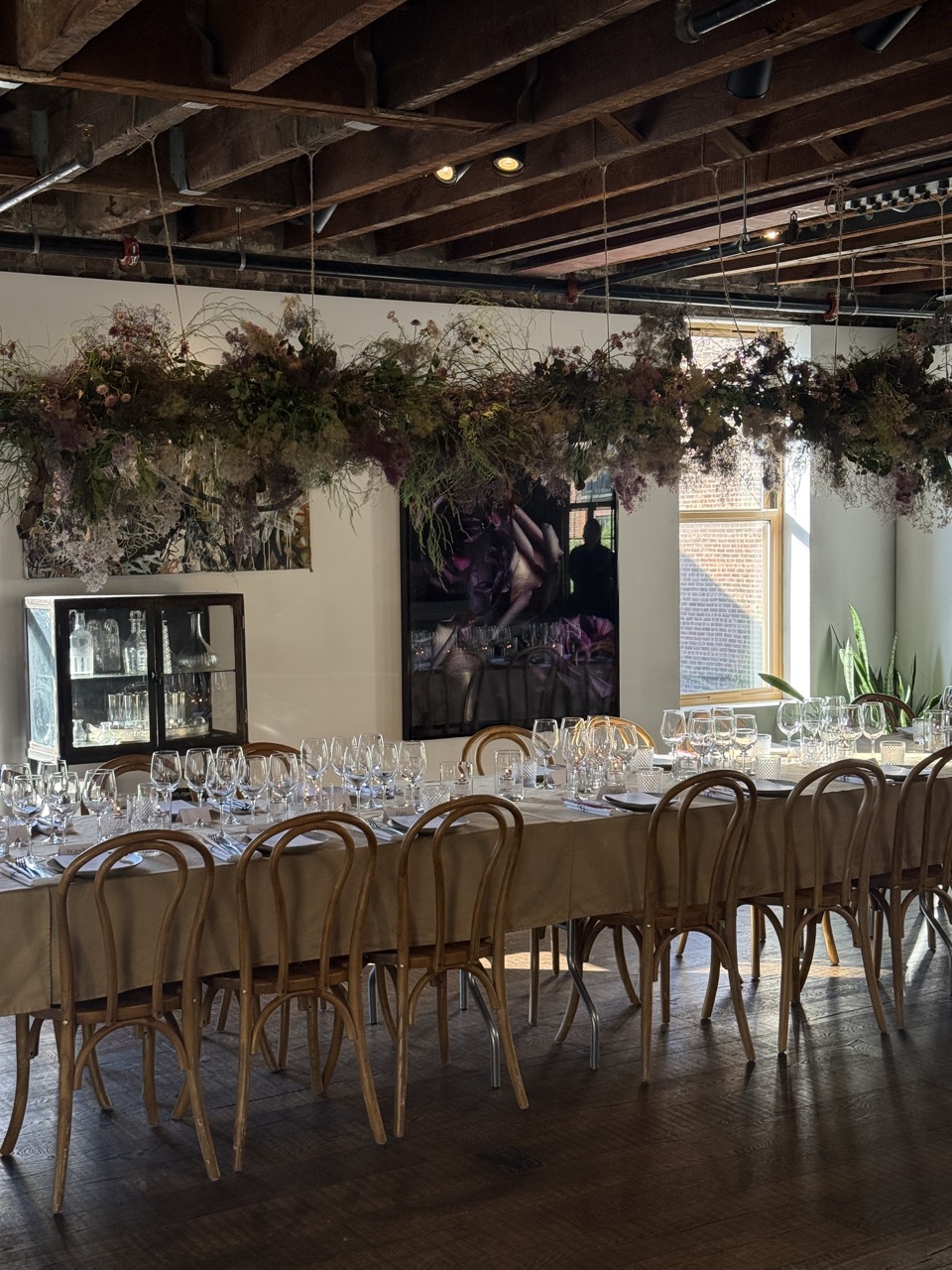 Intimate dinner setting with long tables, candlelight, wooden chairs, and suspended floral installations.